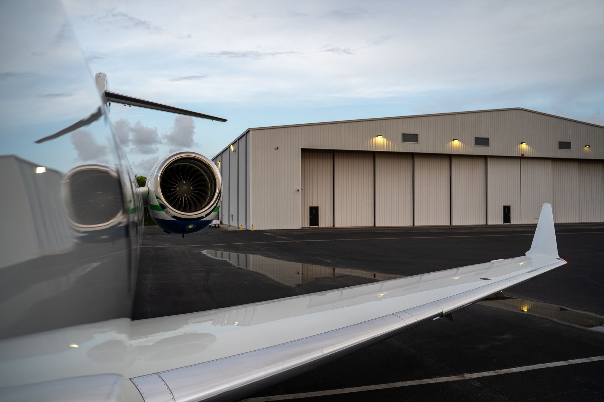 Wing and engine of a CRAFT Challenger on a wet ramp in front of its hangar at dusk
