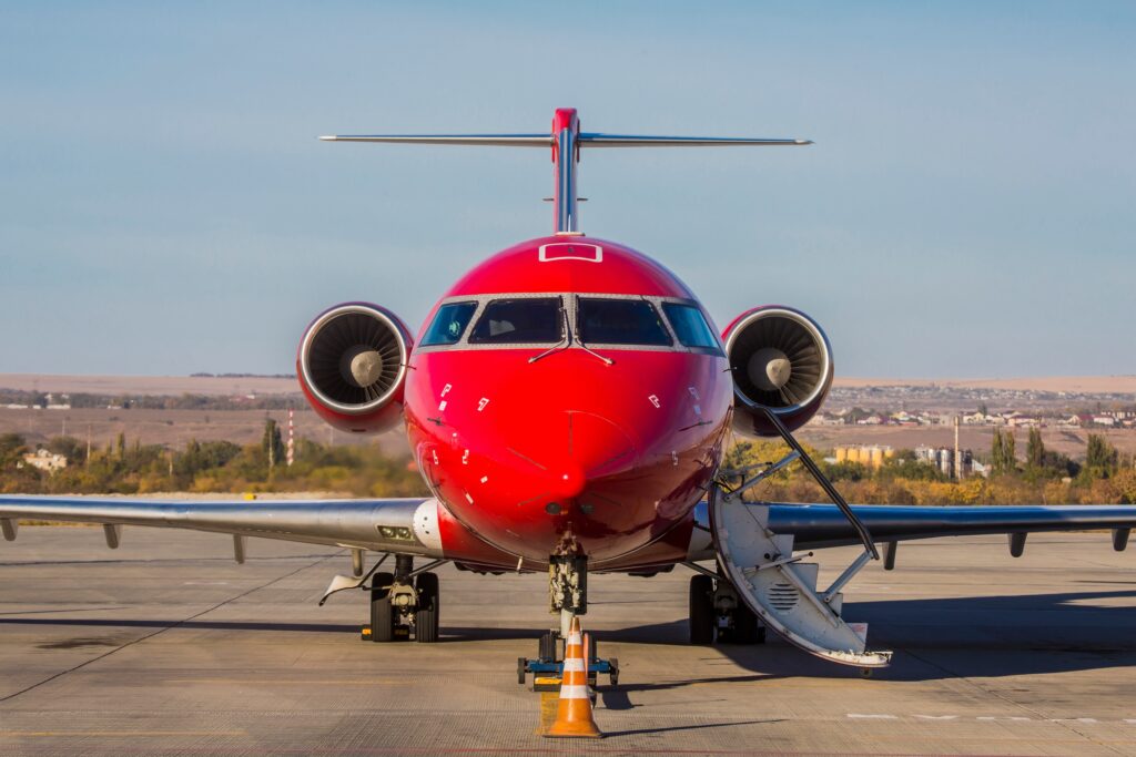 Bright red private jet parked at airport nose on view with stairs extended