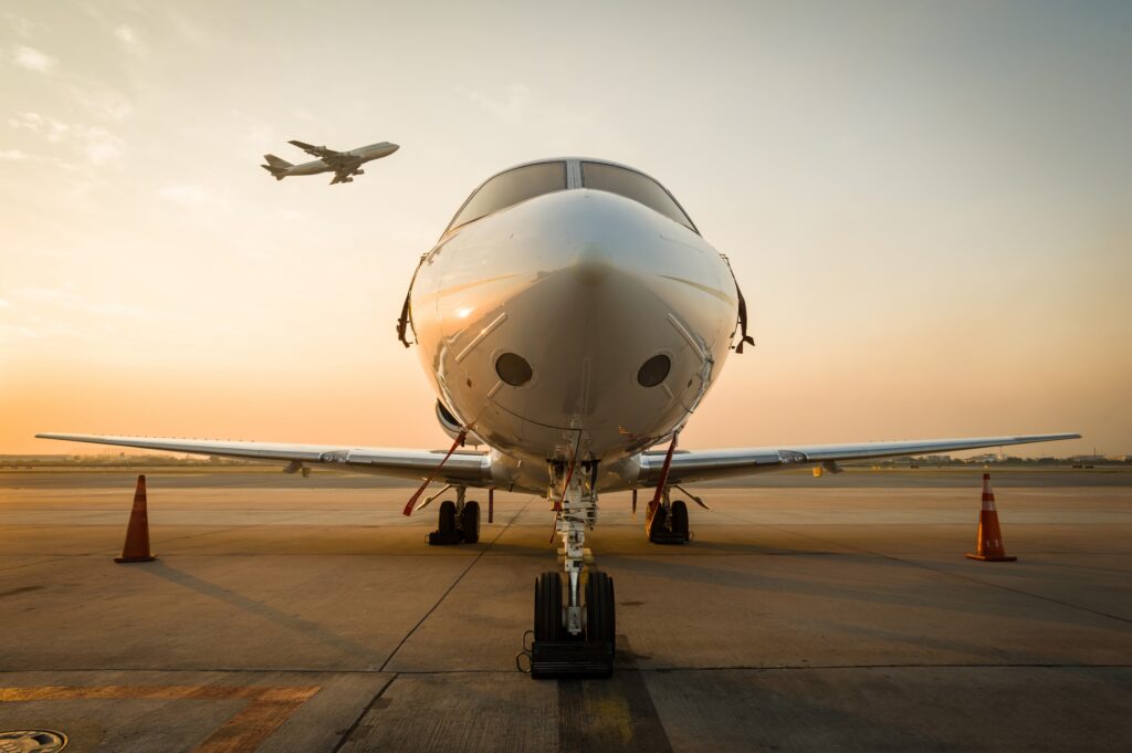 Nose view of private jet parked at airport at sunrise with 747 taking off in the background, considering whether private jets depreciate